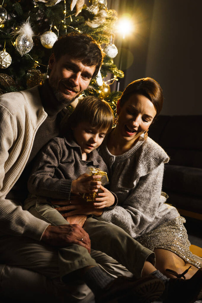 Glückliche Familienväter, Mutter und Sohn schmücken den Neujahrsbaum, haben Spaß, tanzen und packen Geschenke aus. Weihnachten und Silvester. Vertikaler Schuss - Foto, Bild