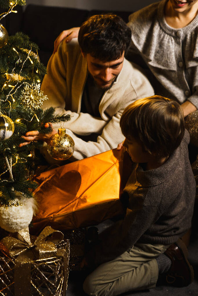 Feliz familia padre, madre e hijo decorar el árbol de Año Nuevo, divertirse, bailar y desempacar regalos. Concepto de Navidad y Año Nuevo. Disparo vertical - Foto, Imagen