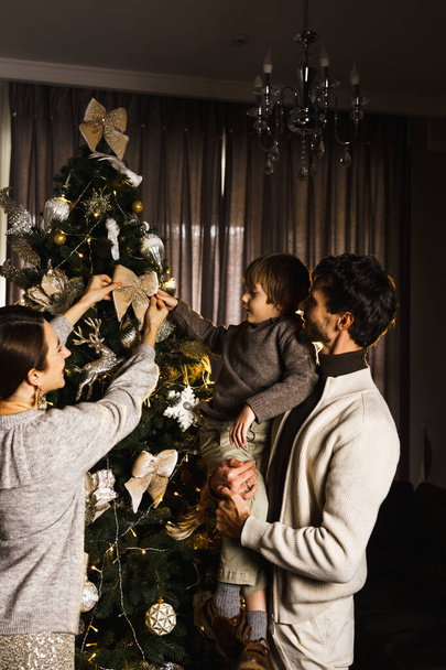 Felice padre di famiglia, madre e figlio decorare l'albero di Capodanno, divertirsi, ballare e disfare i regali. Natale e Capodanno concetto. Colpo verticale - Foto, immagini