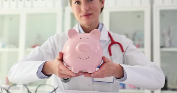 Doctor holds a piggy bank in hands in clinic. Health insurance and treatment costs - Footage, Video