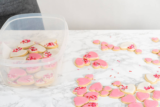 Stockage de biscuits au sucre en forme de cœur avec glaçage royal rose et blanc dans un grand récipient en plastique. - Photo, image