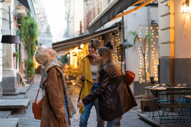 Tres amigos disfrutan de un tranquilo paseo al aire libre, compartiendo risas y conversaciones en un entorno urbano tranquilo durante el otoño.. - Foto, Imagen