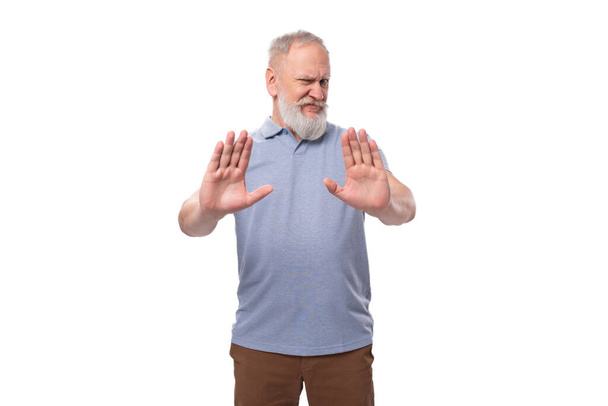 doubtful grandfather with a gray beard and mustache in a t-shirt and trousers on a white background. - Photo, Image