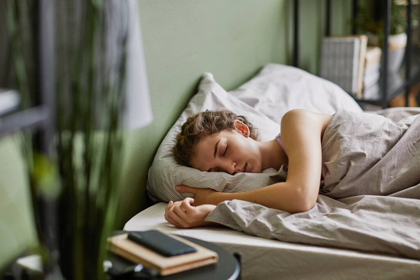 Mujer joven durmiendo en la almohada debajo de la manta en su cama en el dormitorio después de un duro día - Foto, Imagen