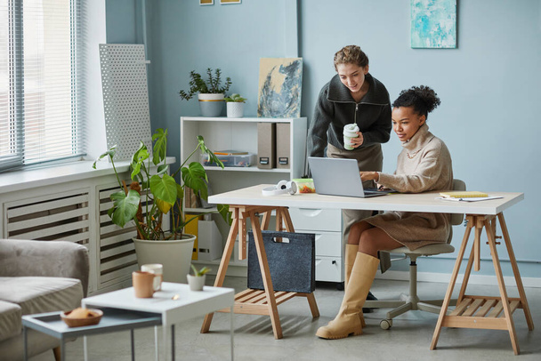 Двое коллег обсуждают дизайн сайта на ноутбуке во время совместной работы в офисе - Фото, изображение