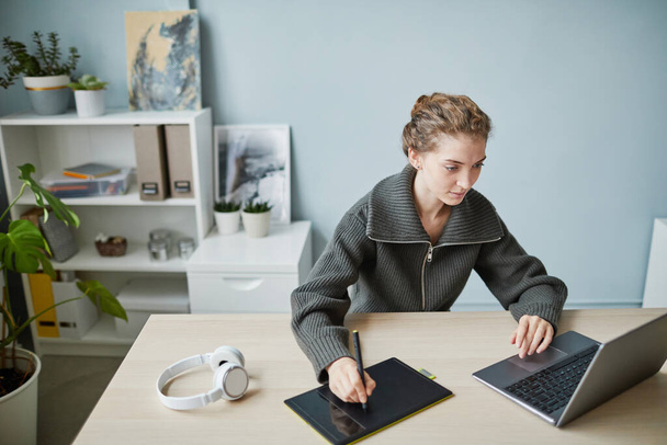 Junge Designerin arbeitet mit Online-Projekt auf Grafik-Tablet an ihrem Arbeitsplatz im Büro - Foto, Bild