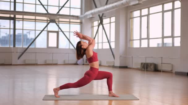 atletisch meisje doen stretching en yoga oefeningen in een studio met grote ramen. naam van de asana Warrior I met Eagle Arm Backbend Virabhadrasana - Video