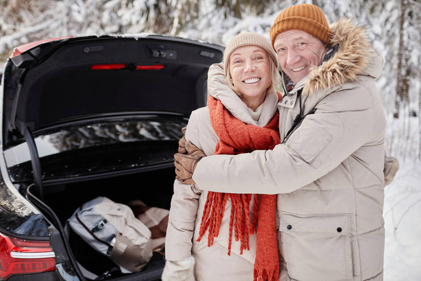 taille omhoog portret van glimlachend volwassen paar genieten van de winter uitje in de natuur terwijl staan door auto kofferbak en kijken naar de camera, kopieer ruimte - Foto, afbeelding