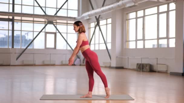 спортивна дівчина робить розтяжку і вправи з йоги в студії з великими вікнами. ім'я Асан Воїн III Вірабхадрасана С - Кадри, відео
