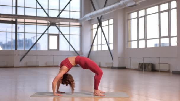 спортивна дівчина робить розтяжку і вправи з йоги в студії з великими вікнами. ім'я асан Одна нога Колесо Eka Pad Urdhva Dhanurasana - Кадри, відео