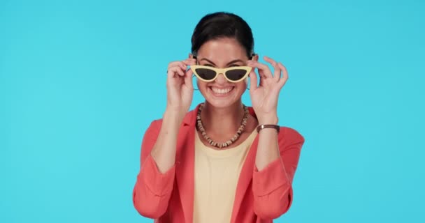 Brille, Mode und Augenzwinkern mit einer Model-Frau im Studio auf blauem Hintergrund für trendigen Stil. Porträt, Brille und verspielter Flirt mit einer glücklichen jungen Frau, die in einem niedlichen Outfit posiert. - Filmmaterial, Video