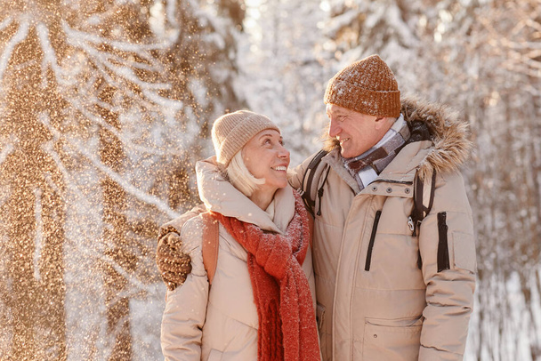 taille omhoog portret van liefdevolle senior paar omarmen in de winter bos met sneeuw vallen - Foto, afbeelding