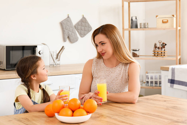 Niña con su madre bebiendo jugo de naranja en la cocina - Foto, Imagen