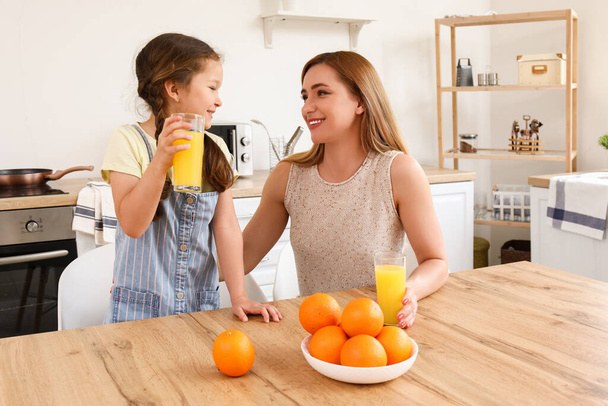Kleines Mädchen mit ihrer Mutter beim Orangensaft in der Küche - Foto, Bild