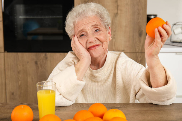 Senior vrouw met sinaasappel en glas sap in de keuken - Foto, afbeelding