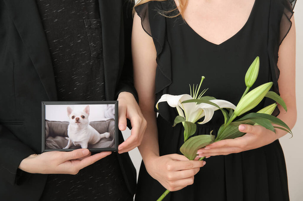 Mujeres sosteniendo marco con imagen de perro y flores de lirio, primer plano. funeral de mascotas - Foto, imagen