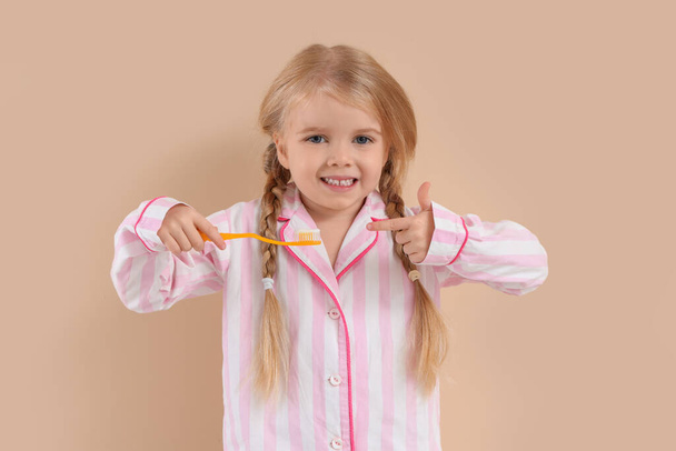 Cute little girl pointing at toothbrush on beige background - Photo, Image