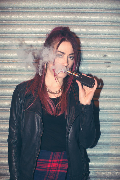 Модная молодая женщина, запыхавшаяся электронной сигаретой
 - Фото, изображение