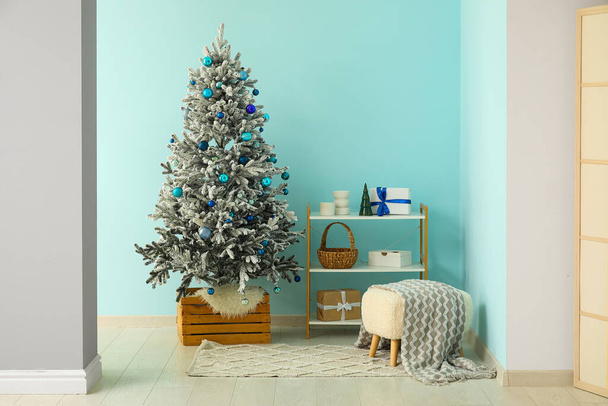 Hermoso árbol de Navidad con estantería y puf cerca de la pared azul - Foto, Imagen