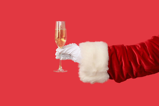 Main de Père Noël avec verre de champagne sur fond rouge, gros plan - Photo, image