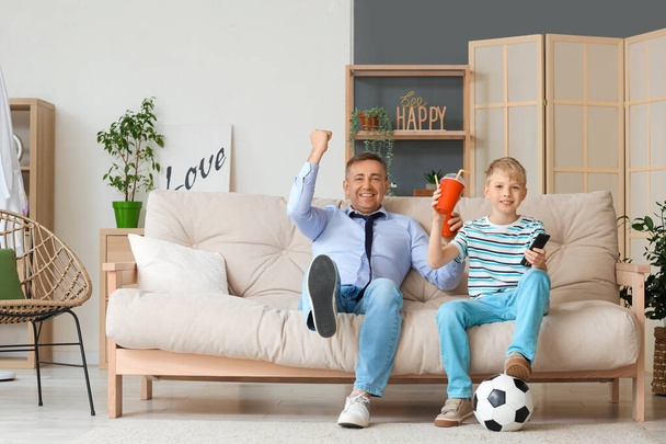 Kypsä lääkäri ja hänen pieni poikansa sooda katsomassa jalkapalloa kotona - Valokuva, kuva