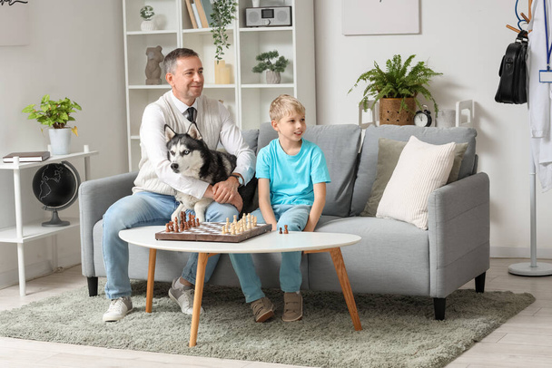 自宅でチェスをする彼の小さな息子とハスキー犬と成熟した医師 - 写真・画像