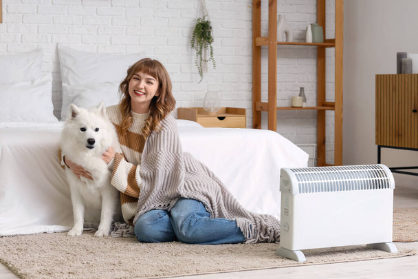 Fiatal nő kockás és Samoyed kutya felmelegedés közelében radiátor a hálószobában - Fotó, kép