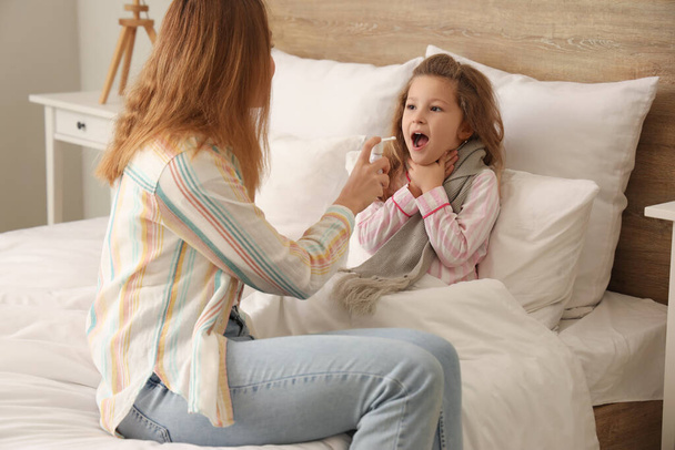Malato bambina con sua madre spruzzando mal di gola in camera da letto - Foto, immagini