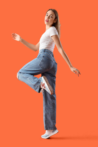 Młoda kobieta w modnych dżinsach na pomarańczowym tle - Zdjęcie, obraz