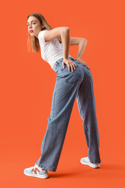 Молодая женщина в модных джинсах на оранжевом фоне - Фото, изображение