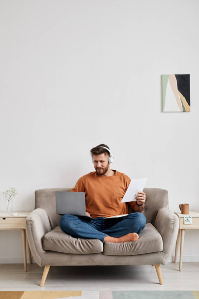 Jovem estudante do sexo masculino em casualwear sentado no sofá e olhando para a tela do laptop enquanto se comunica com o tutor em vídeo chat - Foto, Imagem