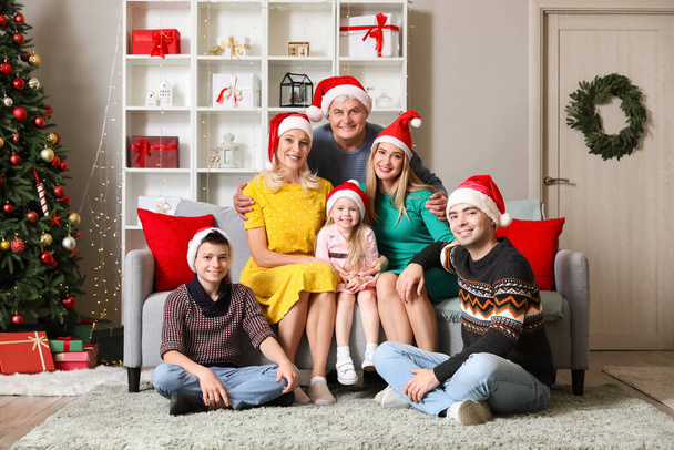 Šťastná velká rodina v Santa klobouky sedí doma na Štědrý večer - Fotografie, Obrázek