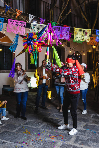Joven latino rompiendo una piñata en tradicional celebración mexicana posada para la víspera de Navidad en México América Latina, familia hispana en días festivos - Foto, Imagen