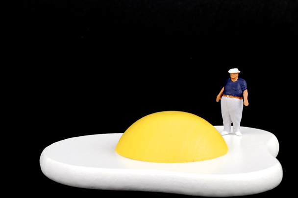 Miniatura di un uomo grasso vicino a un uovo fritto
 - Foto, immagini