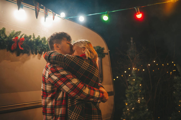 Szczęśliwa para świętująca Boże Narodzenie i Nowy Rok sezon zimowy w Camper Park. Młoda para odpoczynku i relaksu spędzać czas razem uściski i pocałunki w pobliżu przyczepy kempingowej Boże Narodzenie - Zdjęcie, obraz