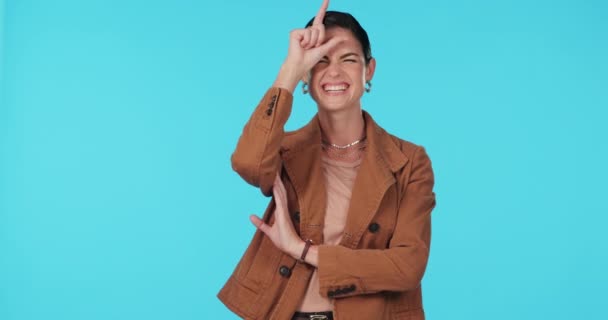 Face, funny and woman with loser sign, review and laughing against a blue studio background. Portrait, female person or model with happiness, symbol of comedy and playing with emoji, smile or opinion. - Footage, Video