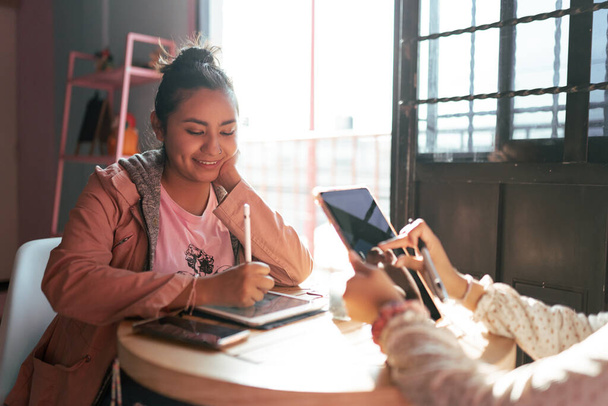 Mladá žena kreslí ve svém digitálním tabletu design, zatímco se stará o svou sestru v kavárně. Koncept práce při hlídání dětí - Fotografie, Obrázek