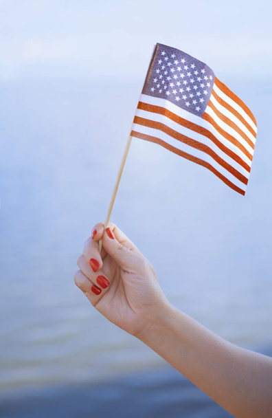 Woman hand holding USA flag in front of the ocean - Photo, Image