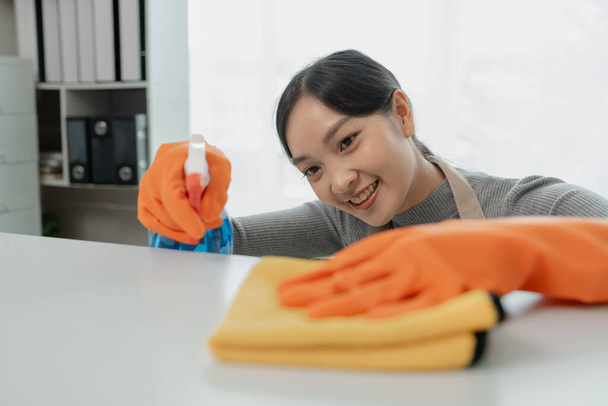 Pulitore femminile asiatico che pulisce i tavoli con spray detergente, la governante sta pulendo la scrivania per l'igiene a causa del Covid-19, idea di pulizia. - Foto, immagini