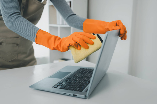Cleaning staff wiping down office equipment, Clean the notebook with a rag, Janitor cleaning the office, Wear rubber gloves and an apron and work with a happy smile,  - Photo, Image