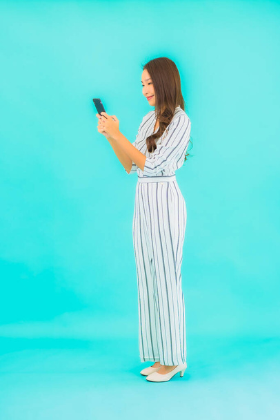 Πορτρέτο όμορφη νεαρή ασιατική γυναίκα χρησιμοποιούν έξυπνο κινητό τηλέφωνο σε μπλε φόντο - Φωτογραφία, εικόνα