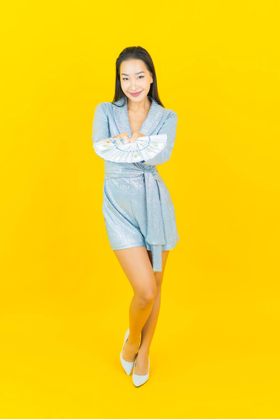 Porträt schöne junge asiatische Frau lächeln mit viel Geld und Geld auf gelbem Hintergrund - Foto, Bild