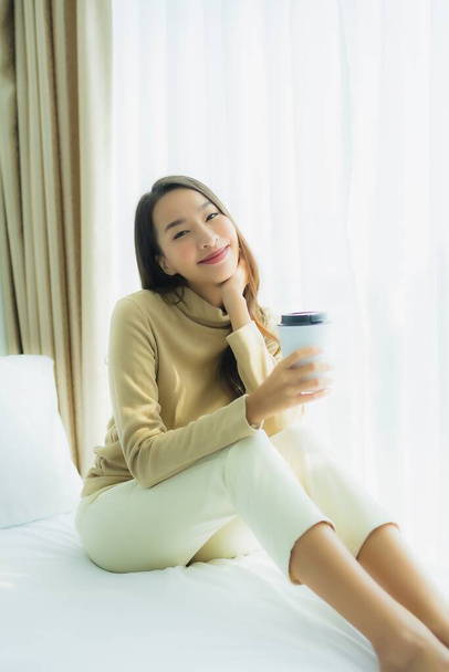 Junge asiatische Frau mit Kaffeetasse auf Bett im Schlafzimmer - Foto, Bild