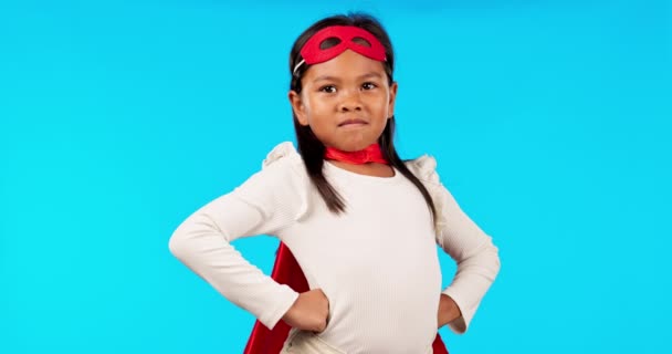 Superheld, sterk en portret van een meisjeskind in een studio met cape en gezichtsmasker met wind. Opslaan, gelukkig en kind model in cosplay outfit of kostuum geïsoleerd door blauwe achtergrond met mockup - Video