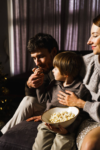 Boldog család ünneplik a karácsonyt, filmeket néznek, popcornt és pizzát esznek az újévi fa mellett. Függőleges fénykép - Fotó, kép