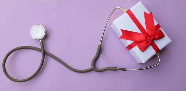 stetoscopio medico con confezione regalo isolata su sfondo viola pastello. concetto natale e capodanno. Foto orizzontale - Foto, immagini