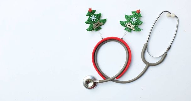ιατρικό στηθοσκόπιο με διακοσμημένο Όμορφη κορδέλα αστεία χριστουγεννιάτικα δέντρα απομονώνουν σε ένα λευκό φόντο. Ιστορικό συγχαρητηρίων στους γιατρούς. Χριστούγεννα ζωής και διακοπές του νέου έτους. - Φωτογραφία, εικόνα