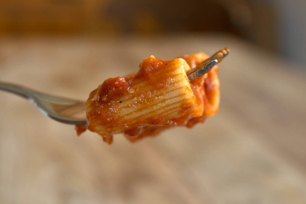 vidlička s rigatoni s rajčatovou omáčkou a v pozadí talíř těstovin s omáčkou - Fotografie, Obrázek
