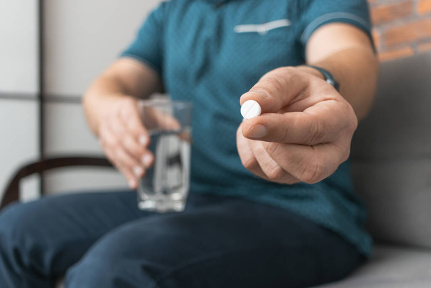 Чоловік приймає ліки, тримає в руці білу терапевтичну таблетку, антибіотики, знеболюючий засіб і склянку води, вид крупним планом. - Фото, зображення