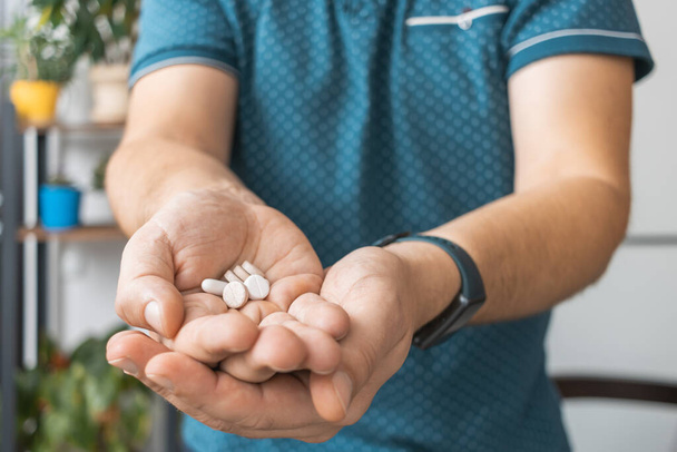 Мужчина держит в руке различные терапевтические таблетки, антибиотики, болеутоляющие, лекарства, крупным планом. - Фото, изображение